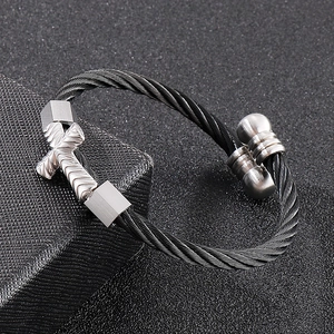 Minimalist stainless steel wire wrapped bracelet with silver cross accent on grey surface