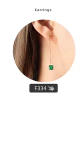 Detail of a long gold drop earring with a delicate chain and a square green gemstone