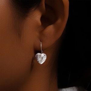 Macro shot of silver heart drop earrings with faceted clear crystal on model's ear
