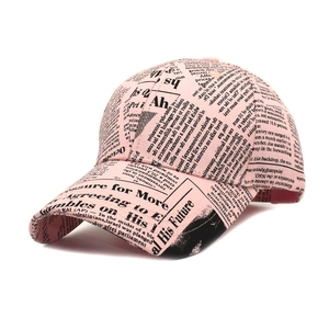 Detail of pink baseball cap featuring black newspaper print and curved brim on white background