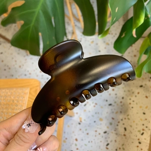 Close-up of a large glossy dark brown hair claw clip held by a hand in lifestyle setting