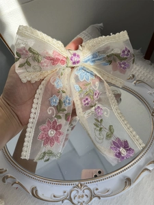 Detail of delicate floral embroidery on lace bow hairclip with pastel flower patterns