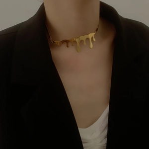 Detail of a liquid drop design gold necklace worn over a black blazer and white shirt