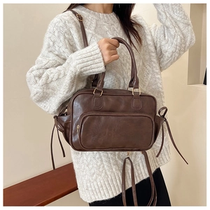 Detail view of a vintage caramel brown leather bag with adjustable strap on a white sweater