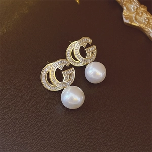 Macro view of gold plated double G earrings with clear zircons and round white faux pearls