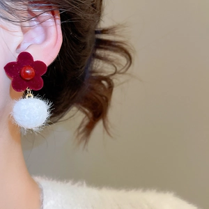 Close-up of red flocked flower and white pom-pom earring on a model for autumn style