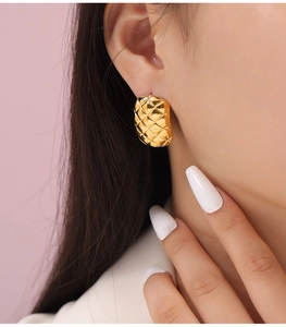 Close-up of golden rhombus pattern earrings with polished metallic texture on model