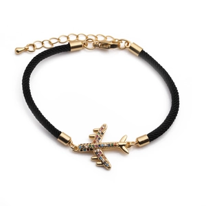 Macro shot of gold airplane charm with colorful crystals on black woven bracelet cord