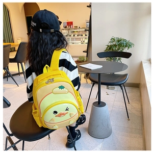 Toddler cartoon yellow duck backpack with 3D wings shown on child in a cozy cafe