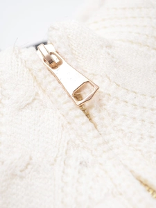 Detailed macro view of the golden geometric zipper on a thick white knitted jacket