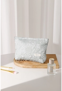 Detailed view of silver jacquard makeup bag with floral relief and H&R logo tag