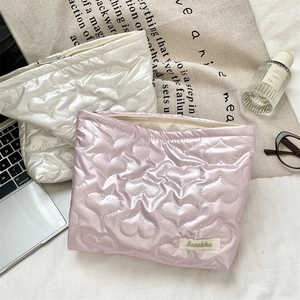 Detail of heart quilted PU leather pouches in pearl white and pink on a textured desk