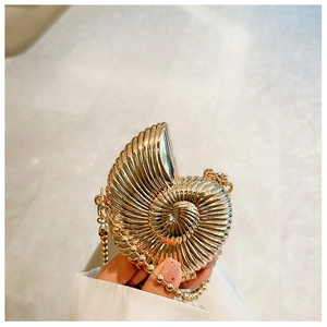 Detail of a golden seashell handbag with high-gloss metallic finish and beaded chain strap