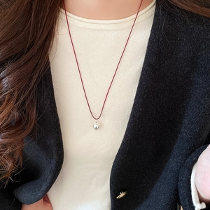 Detail of red cord necklace with polished silver apple pendant on white knit sweater