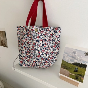 Floral canvas mini handbag with red ribbon handles and metal snap closure on a white shelf
