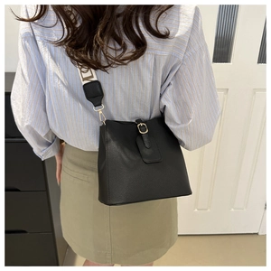 Detail of black pebbled leather bucket bag with wide logo strap and gold buckle