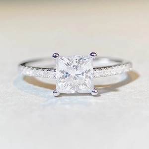 Macro shot of princess cut moissanite diamond with side stone accents on silver band