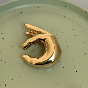 Détail d'une broche en métal doré poli en forme de geste OK sur une assiette en céramique