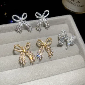 Sparkling zircon bow jewelry set with gold and silver earrings on a gray display tray