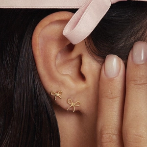 Elegant gold bow-shaped stud earrings with bead details worn by a model in a close-up view