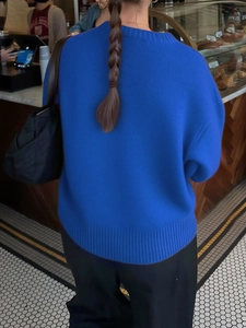 Back view of a blue round neck long sleeve knit sweater with ribbed cuffs in a cozy cafe