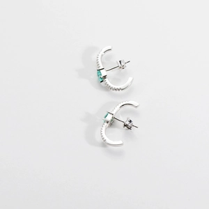 Detailed close-up of C-shaped silver stud earrings featuring green emerald and cubic zirconia