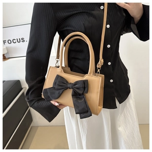 Detail of beige PU leather crossbody bag featuring a large black satin bow decoration