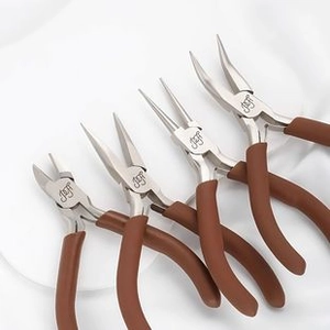 Macro view of four professional jewelry pliers with brown anti-slip handles on white fabric