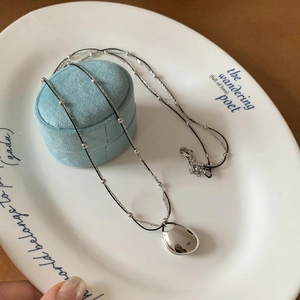 Minimalist silver chain necklace with a bean pendant on a ceramic dish with velvet box