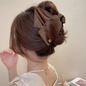 Detail of a large brown satin bow hair claw clip with gold accents on model's hair