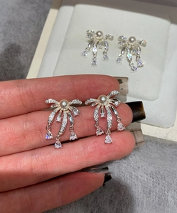 Detail of silver bow earrings with rhinestone tassels and a central pearl drop