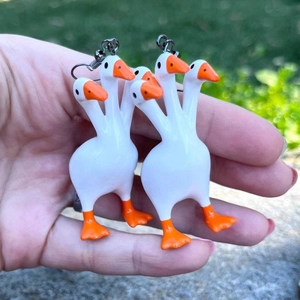 Close-up of creative three-headed goose earrings in glossy white finish held by hand