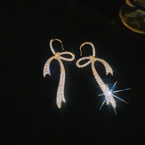 Close-up of gold plated bow earrings with sparkling zircons on black velvet background