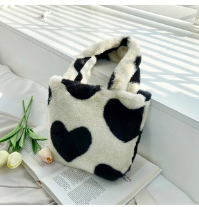 Plush bucket bag with black heart pattern placed on a book with white tulips decoration