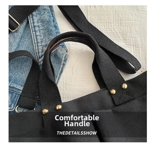 Detail of reinforced black canvas tote handles with gold metal rivets and shoulder strap