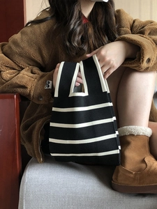 Close-up of black and white striped knit tote bag held by a model in a cozy indoor setting