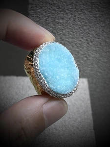Macro shot of adjustable gold ring featuring a light blue druzy stone with small crystals