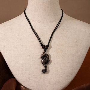 Detailed close-up of a Maori style resin seahorse pendant on a black woven cord necklace