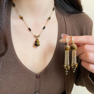 Detail of tiger eye hulu necklace and tassel earrings set on a model with gold finish