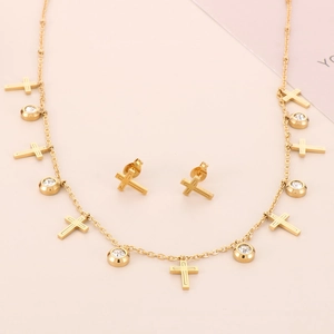 Detailed close-up of golden cross necklace and stud earrings set with clear gemstones