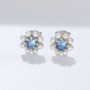 Macro detail of silver flower earrings with blue zircon center and white pearls