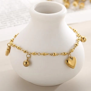 Detail of golden stainless steel beaded anklet with heart charms on white ceramic vase