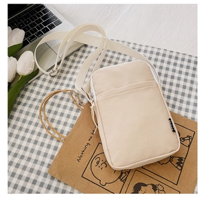 Close-up of beige corduroy crossbody bag with adjustable strap on a plaid background