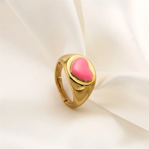 Close-up of golden copper ring featuring pink enamel heart on elegant white silk