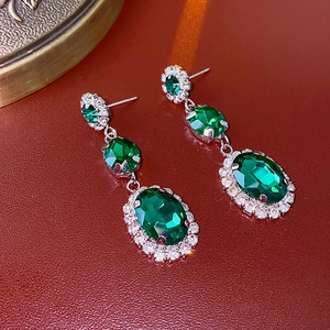 Detailed macro view of silver earrings featuring emerald green stones and diamond accents