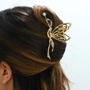 Detail of a golden butterfly metal hair claw clip with a pearl accent worn by a model