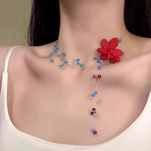 Nahaufnahme einer roten Stoffblume und blauer Perlen an einer transparenten Halskette