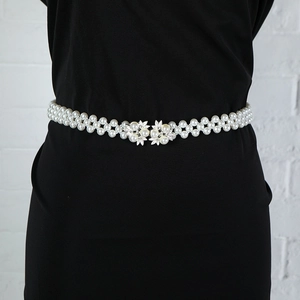 Detail of elegant double-row pearl waist chain with leaf-shaped rhinestone buckle on black dress