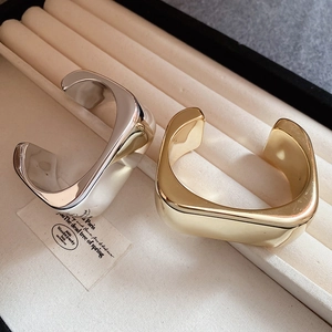 Minimalist wide irregular wave bangles in gold and silver finish on a jewelry box