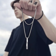 Close-up of a hand holding a polished silver cylinder pendant on a sleek necklace chain